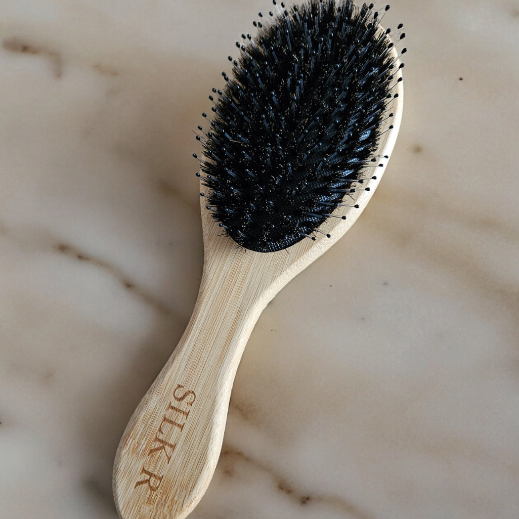 brosse en bambou beige à poils de sanglier et nylons posé sur un fond en marbre