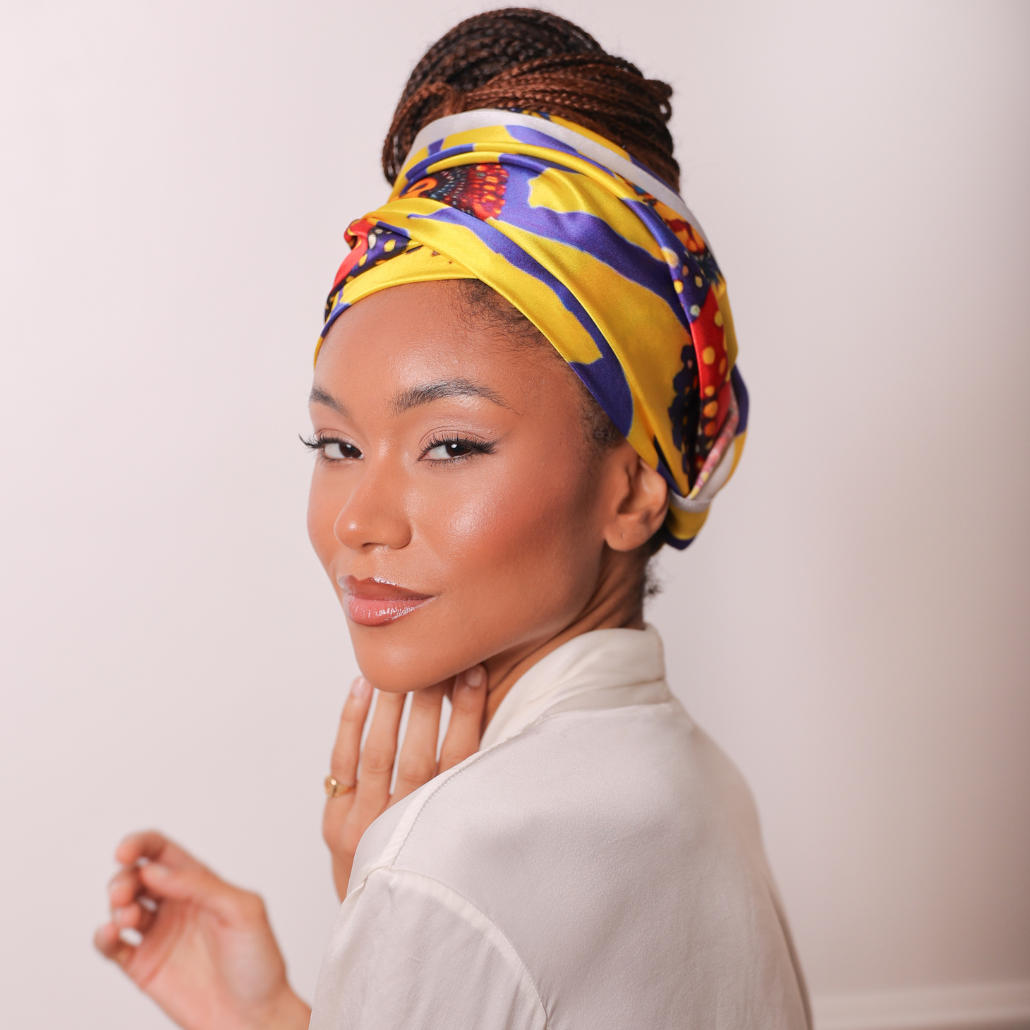 Femme qui porte un carré de soie imprimé wax couleur jaune, rouge et bleu, elle le porte en bandeau autour de ses braids attachées en chignon