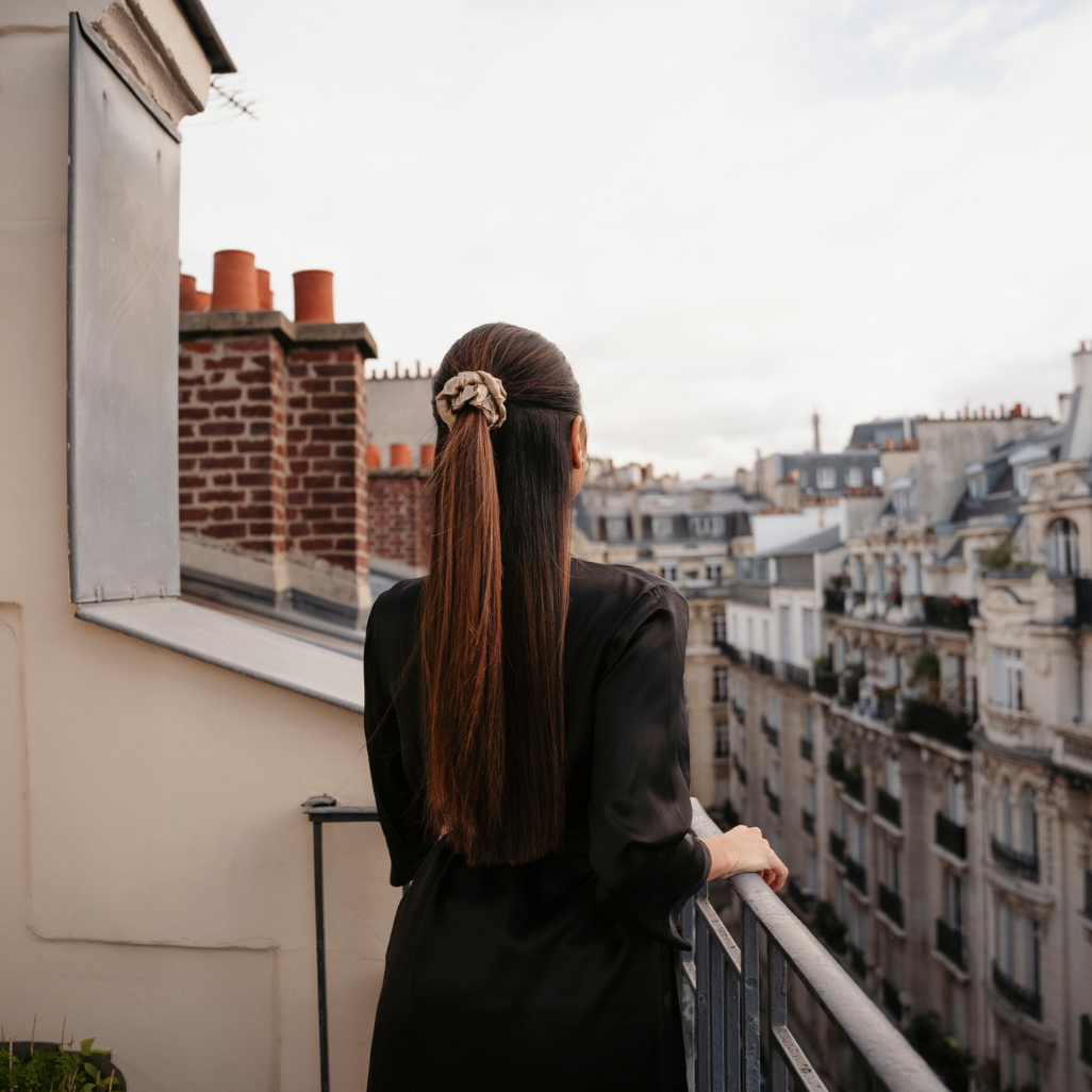 Femme qui pose de dos sur un balcon parisien les cheveux attachés en demi queue avec un chouchou de couleur ivoire