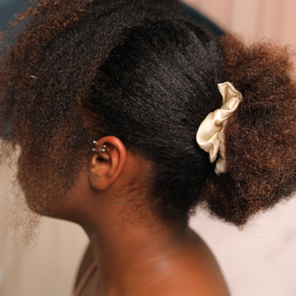 femme qui pose de profil avec les cheveux afros les cheveux attachés avec un chouchou de couleur de champagne