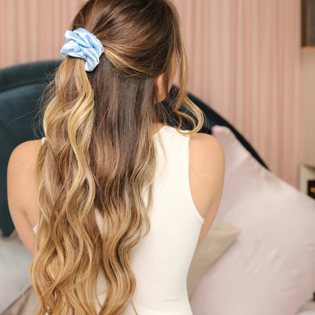 Femme blonde qui pose de dos avec les cheveux longs attachés d'un chouchou de couleur bleu ciel