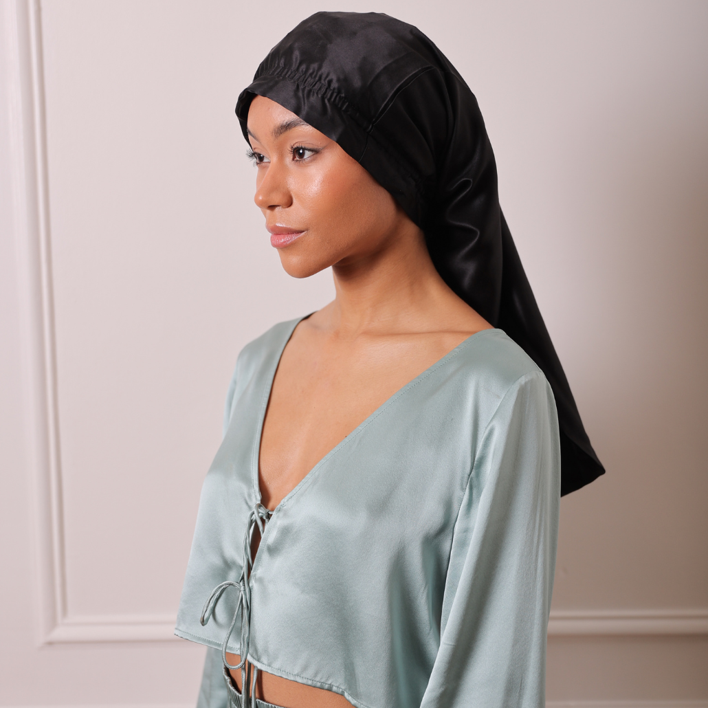 Femme qui porte un bonnet de protction long noir pour la nuit elle pose de face avec un pyjamas en soie de couleur vert sauge