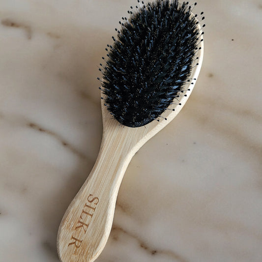 brosse en bambou beige à poils de sanglier et nylons posé sur un fond en marbre