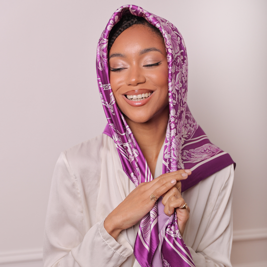 Femme qui porte un carré de soie sur la tête de couleur violet et blanc et qui affiche un joli sourire 